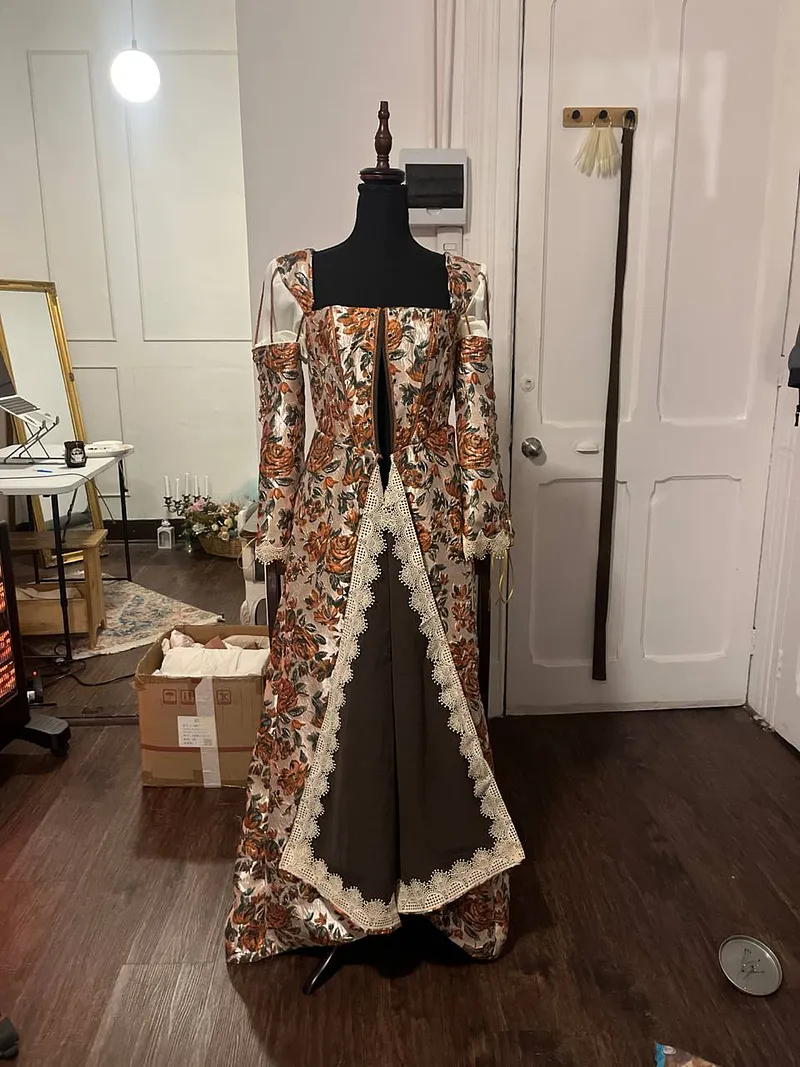 Vista frontal del vestido sobre maniquí, con sobrefalda floral abierta, panel central oscuro y encaje claro siguiendo los bordes.