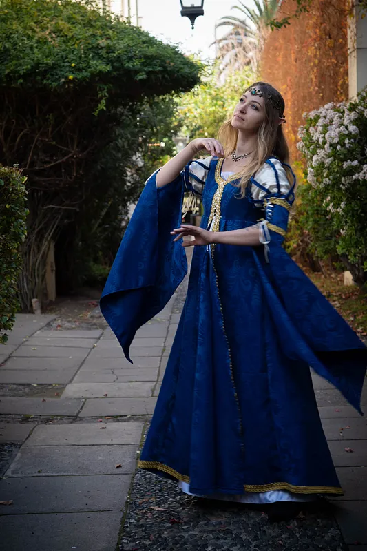 Vista en movimiento del vestido azul, con falda extendida, mangas abullonadas a rayas y largos paneles laterales ribeteados en dorado.