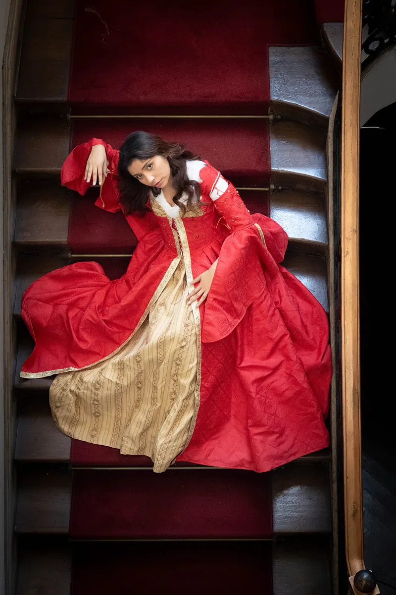 Vestido rojo y dorado sobre una escalera antigua, una referencia visual para una presencia de corte barroca.
