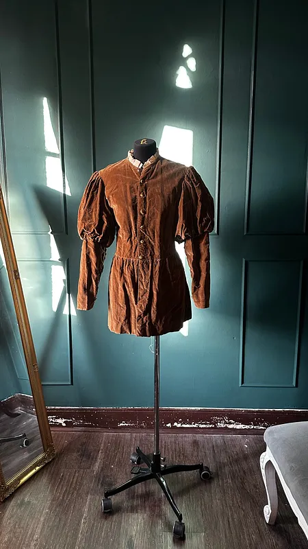 Vista frontal de la chaqueta ocre sobre maniquí, con botones centrales, hombros fruncidos y faldón por debajo de la cadera.