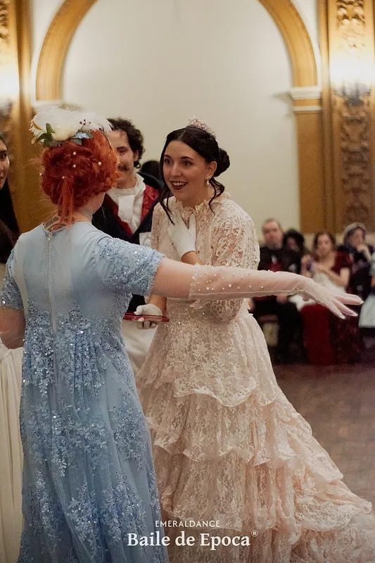 Escena de baile donde se aprecia desde atrás el vestido celeste bordado, con mangas cortas y guantes transparentes hasta el codo.