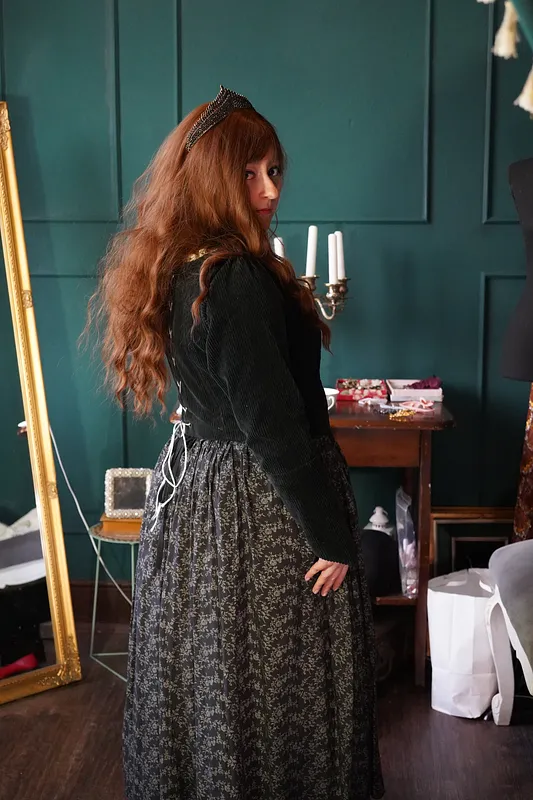 Vista posterior de tres cuartos del vestido, con lazo blanco de ajuste en la espalda, cabello largo sobre el cuerpo negro y falda floral amplia.