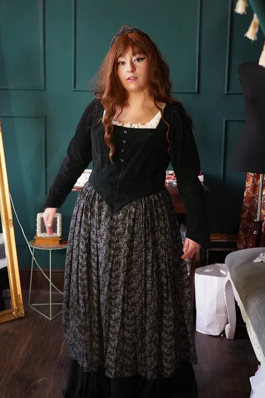 Vista frontal media del vestido, con detalle del corpiño negro texturado, cintura en punta, escote claro fruncido y falda floral.