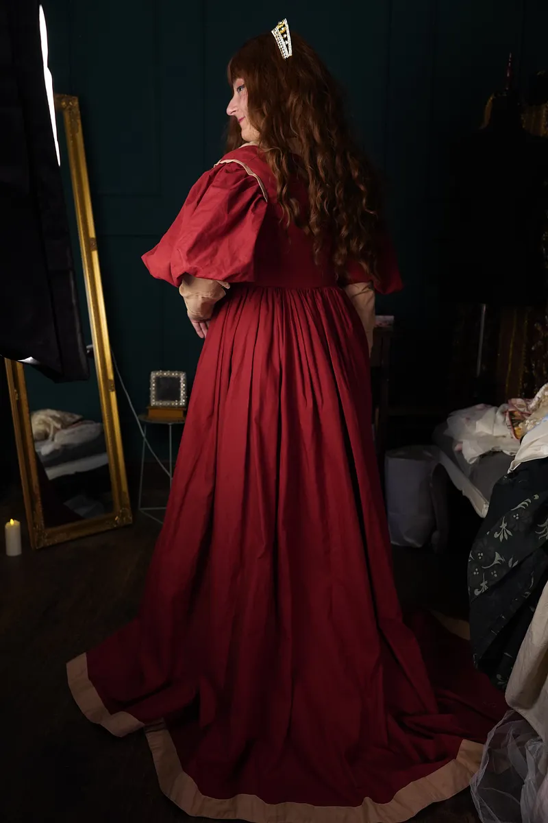 Vista posterior del vestido, con espalda roja lisa, falda larga de gran volumen, borde beige y tocado brillante visible.