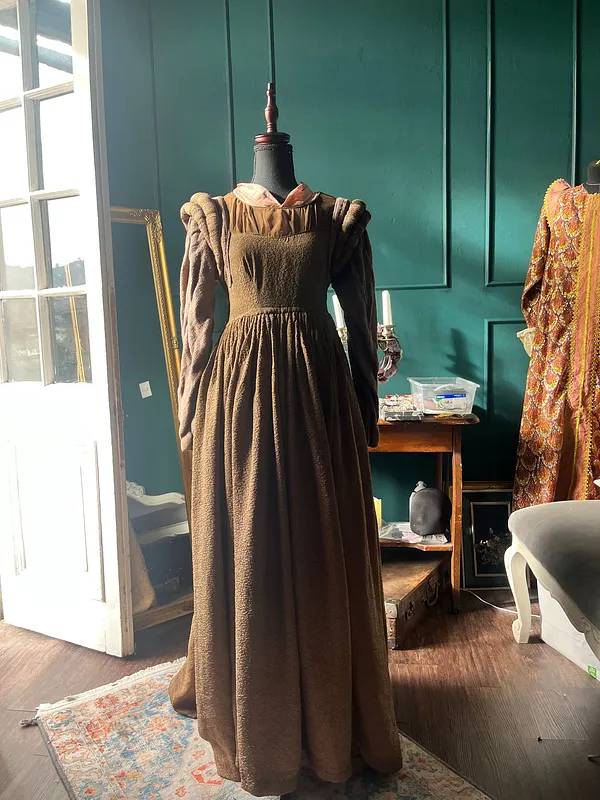 Vista frontal de un vestido largo café, con corpiño entallado, escote cuadrado, hombros fruncidos y mangas largas ajustadas.