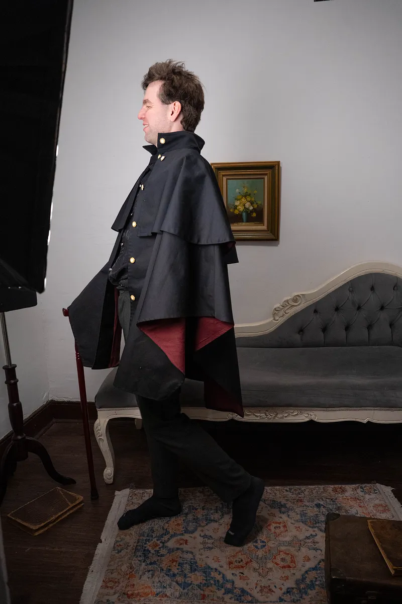 Edgar (abrigo) en negro, fotografiado de perfil con una silueta larga y sobria para un look gótico de fantasía.
