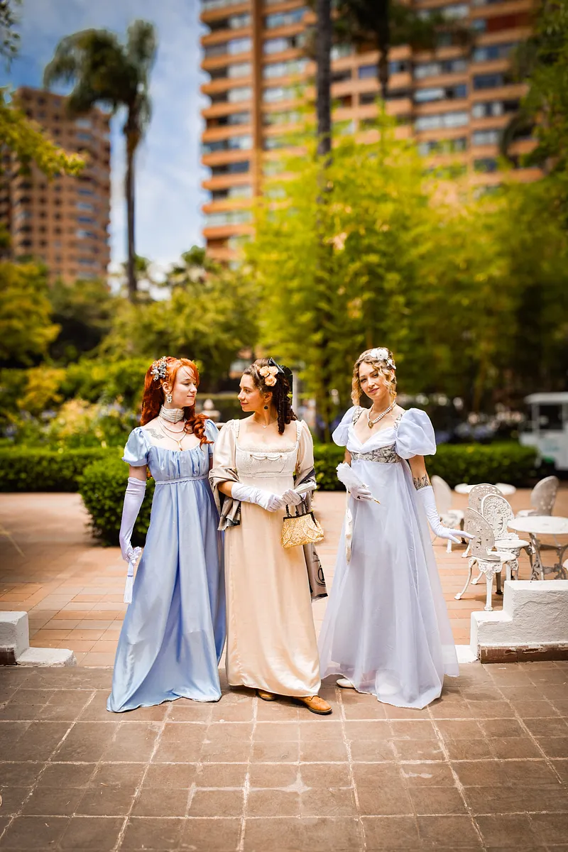 Goldie junto a otros vestidos claros en una celebración al aire libre inspirada en Jane Austen, mostrando cómo se lee una silueta romántica dentro de un grupo.
