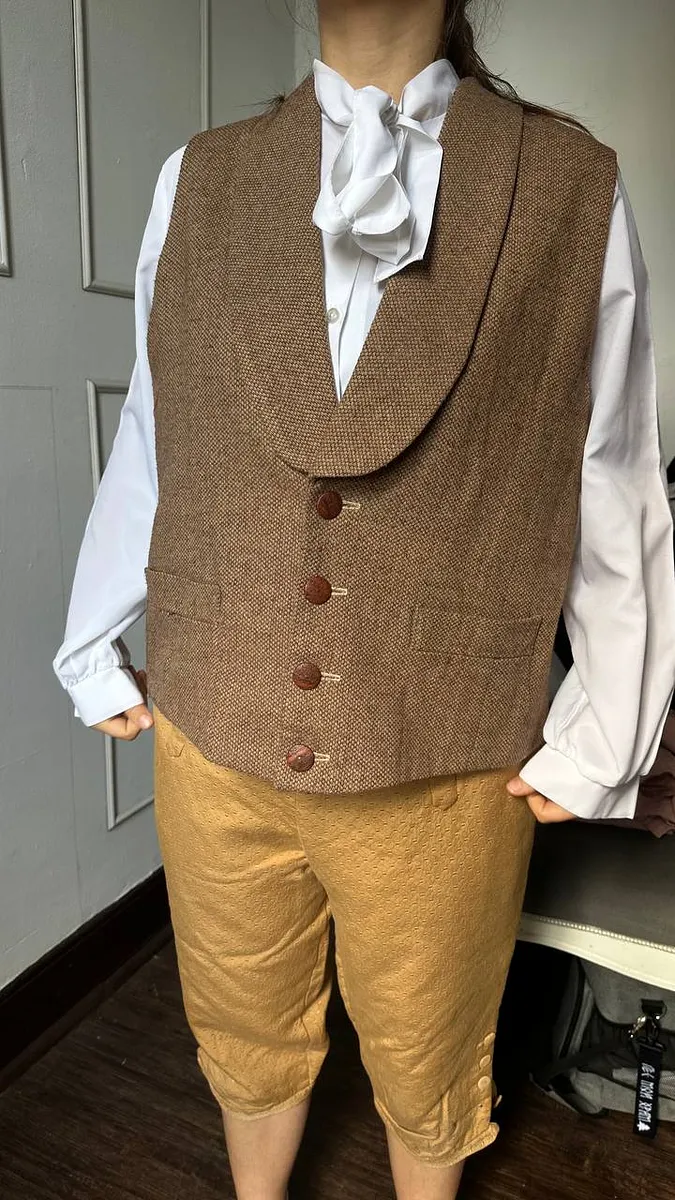 París con camisa blanca de cuello alto, chaleco café y pantalón corto en una combinación masculina inspirada en fines del siglo XVIII.