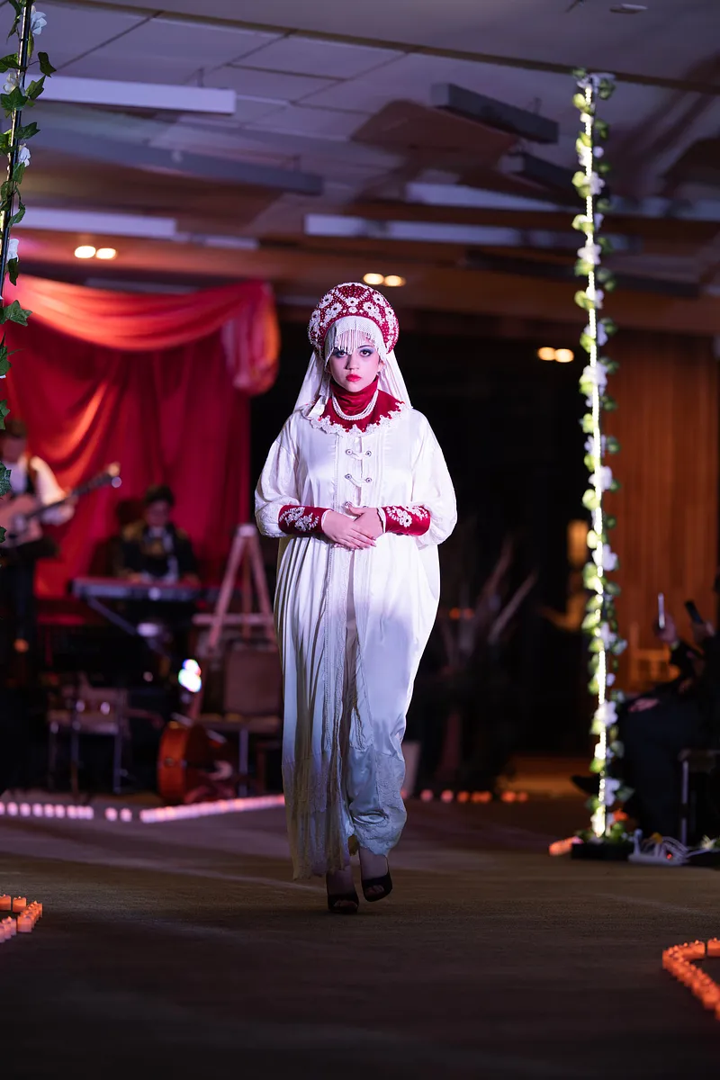 Emperatriz Blanca en pasarela, con vestido claro, detalles rojos y tocado alto de inspiración rusa.