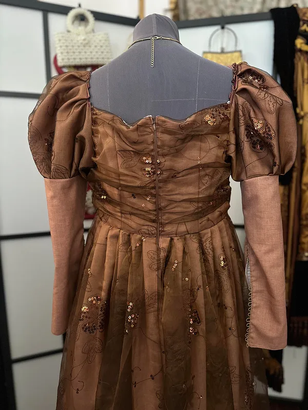 Parte posterior del vestido en maniquí, con cierre central, espalda de escote amplio, mangas abullonadas y puños largos en tono rosado.