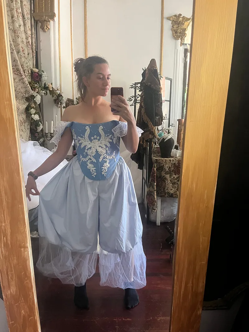 Vista frontal en espejo de un vestido celeste y blanco, con falda amplia, corpiño azul bordado y mangas cortas abullonadas.