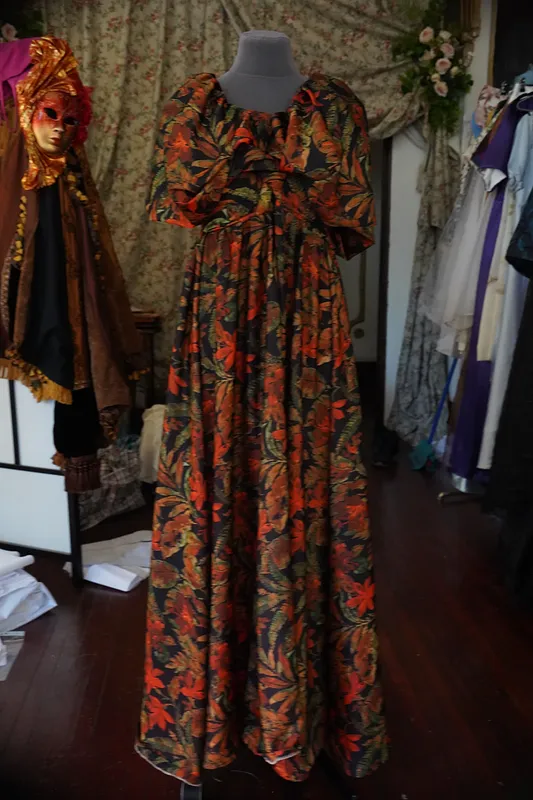 Vestido floral largo presentado sobre maniquí, con abundantes motivos rojos y verdes distribuidos desde el cuerpo hasta la falda.
