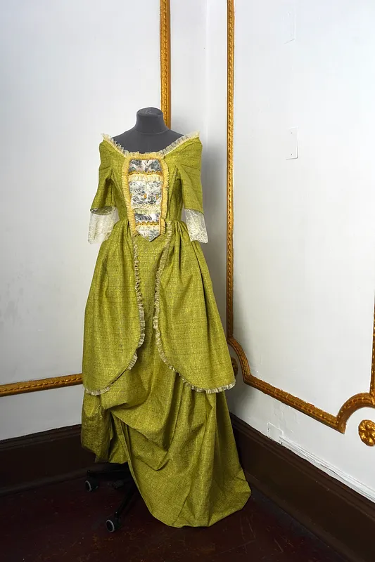 Vista frontal sin antifaz del vestido sobre maniquí, destacando el escote amplio, las mangas con encaje claro, el panel decorado del torso y la falda larga recogida.