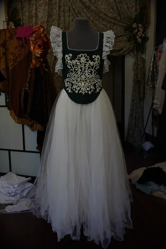 Vestido Annie en maniquí, visto de frente, con escote cuadrado, corpiño verde oscuro bordado en blanco y falda larga de tul blanco.