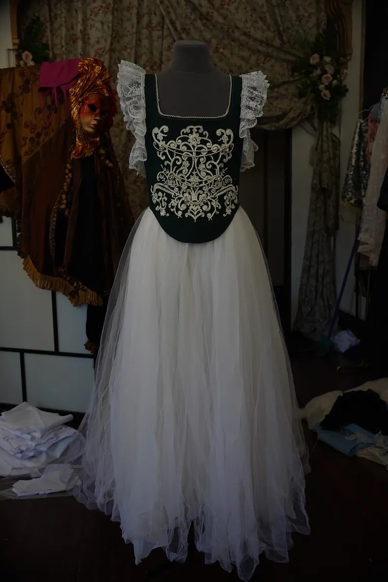 Vestido Annie en maniquí, visto de frente, con escote cuadrado, corpiño verde oscuro bordado en blanco y falda larga de tul blanco.