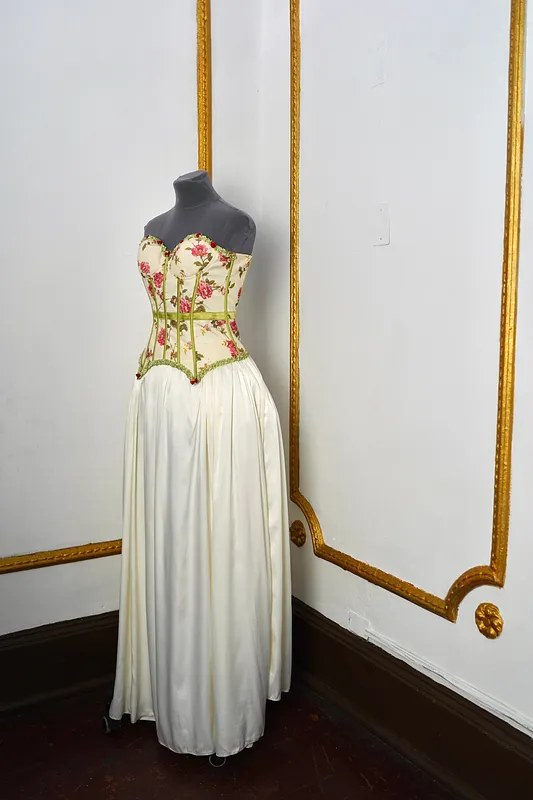 Vista en tres cuartos del vestido, mostrando el escote corazón, el estampado de rosas del corset y la caída fruncida de la falda marfil.