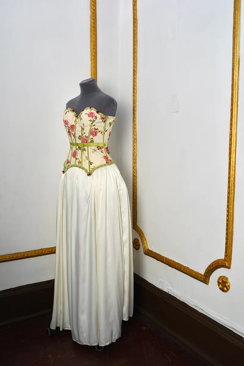 Vista en tres cuartos del vestido, mostrando el escote corazón, el estampado de rosas del corset y la caída fruncida de la falda marfil.