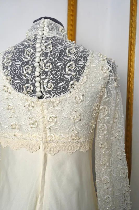 Detalle posterior superior del vestido, con encaje floral transparente, perlitas decorativas, botones forrados en la espalda y terminación de encaje en la cintura.