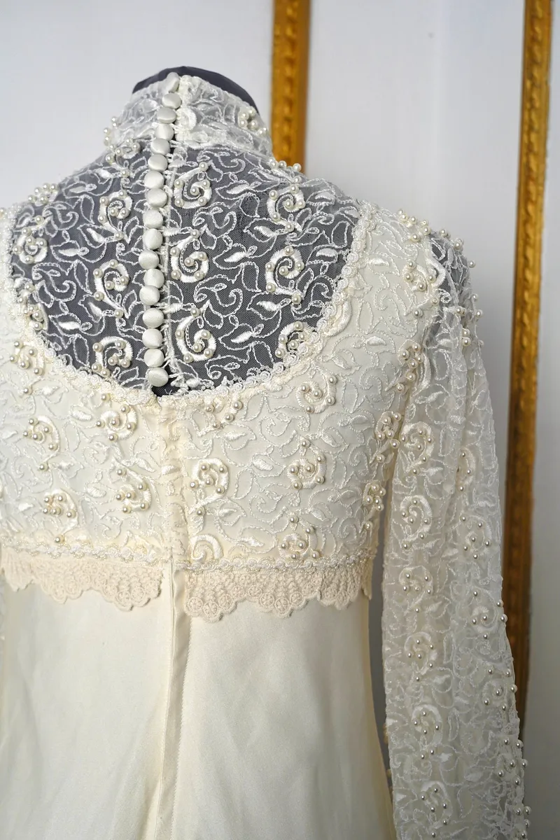 Detalle posterior superior del vestido, con encaje floral transparente, perlitas decorativas, botones forrados en la espalda y terminación de encaje en la cintura.