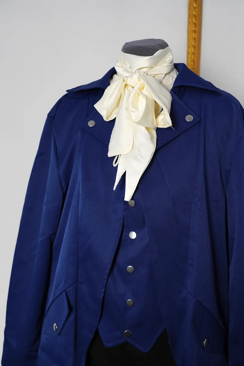 Detalle superior del conjunto con solapas azules, botones metálicos, chaleco a juego y pañuelo crema anudado alrededor del cuello.