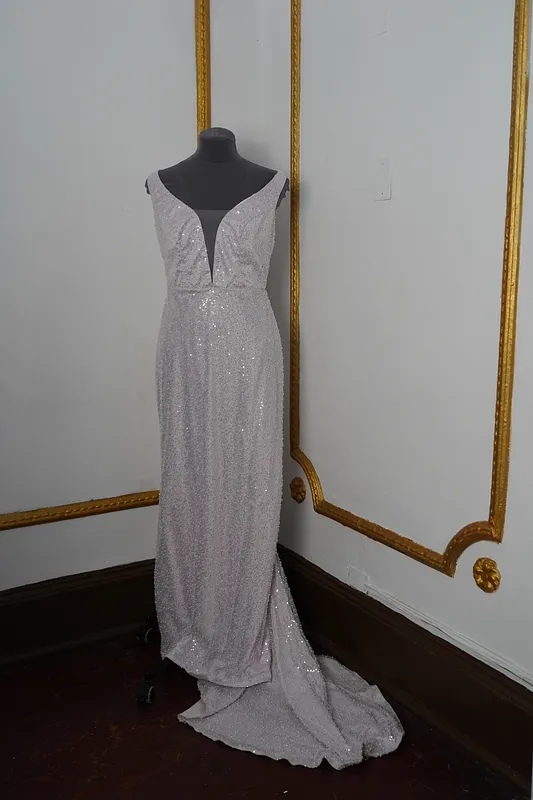 Vista frontal completa del vestido en maniquí, con tirantes anchos, escote profundo, falda larga plateada brillante y cola recogida hacia un costado.