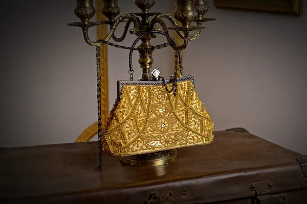 Bolso estructurado de brocado dorado, con motivos ornamentales, marco metálico y dos asas cortas sobre una superficie oscura.