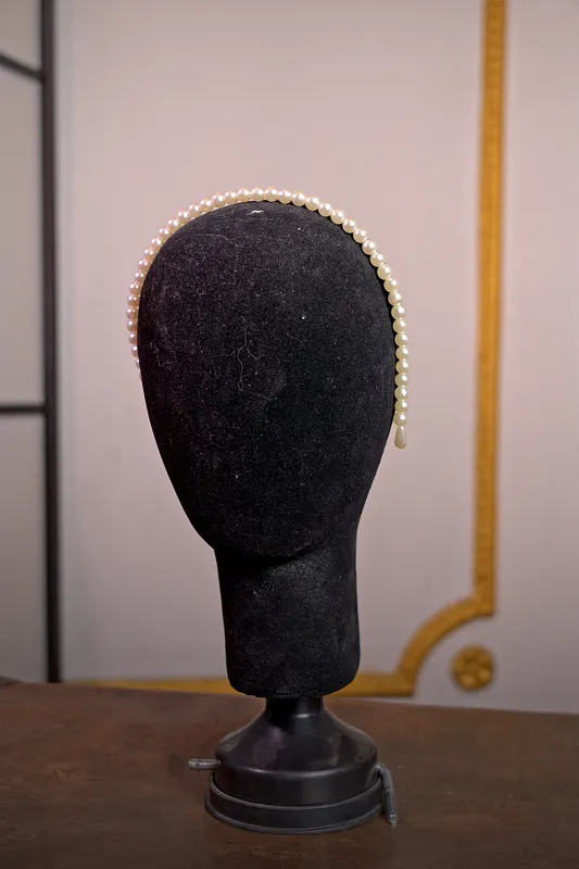 Delgada diadema cubierta de pequeñas perlas claras, vista de perfil sobre una cabeza de maniquí negra.