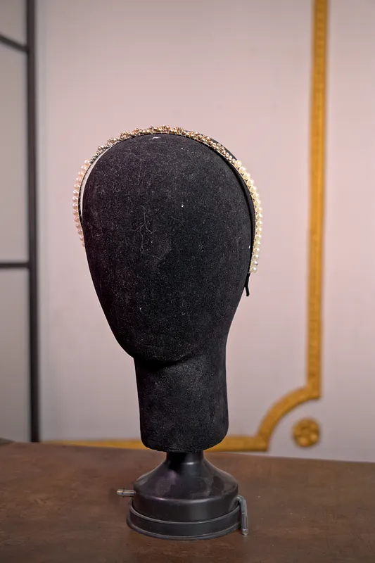 Diadema metálica delgada sobre soporte negro, de tono dorado envejecido y contorno sencillo, sin piedras ni adornos prominentes.