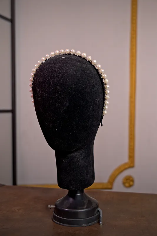 Diadema sencilla cubierta por una hilera uniforme de perlas blancas, presentada sobre un soporte de terciopelo negro.