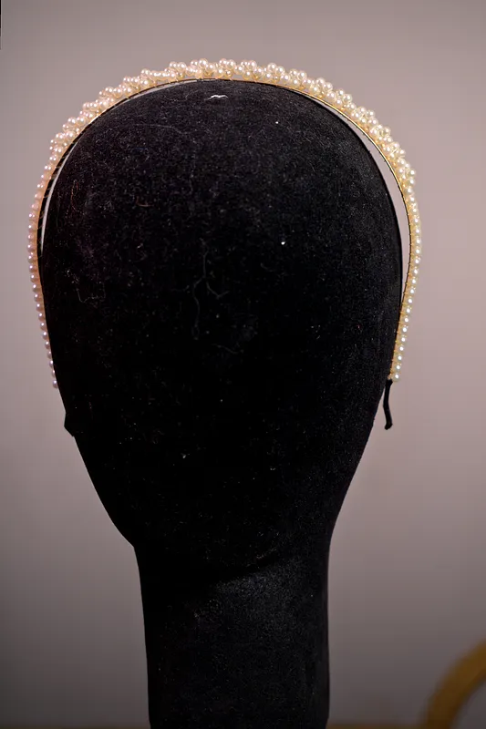 Primer plano de una diadema angosta cubierta por dos hileras de pequeñas perlas claras sobre cabeza de maniquí.