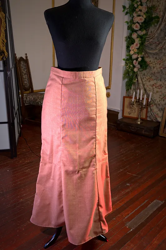Falda larga color coral sobre maniquí, de cintura alta y corte levemente acampanado, con abertura formada por paneles delanteros.