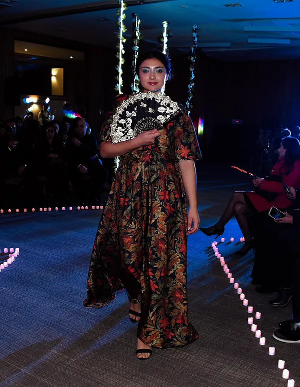 Modelo en pasarela con vestido floral largo y chal negro con bordados blancos, mostrado de frente bajo iluminación nocturna.