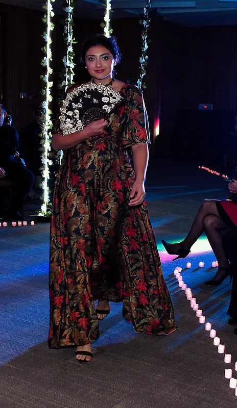 Vista frontal en pasarela del vestido oscuro con estampado floral rojo, mangas abullonadas y falda recta hasta los tobillos.