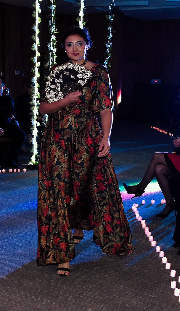 Vista frontal en pasarela del vestido oscuro con estampado floral rojo, mangas abullonadas y falda recta hasta los tobillos.