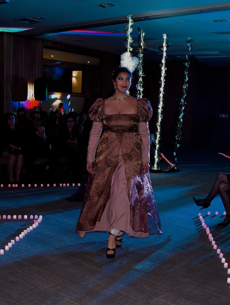 Modelo caminando en pasarela con el vestido Lilian, donde se distingue la sobrefalda cobriza, la falda interior rosada y las mangas abullonadas.