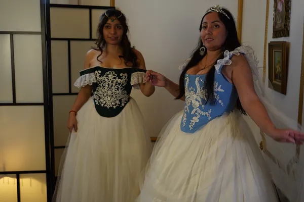 Dos mujeres posan con vestidos de fantasía de corsé bordado y falda blanca; a la derecha, el diseño celeste se complementa con velo, tiara y mangas de tul.
