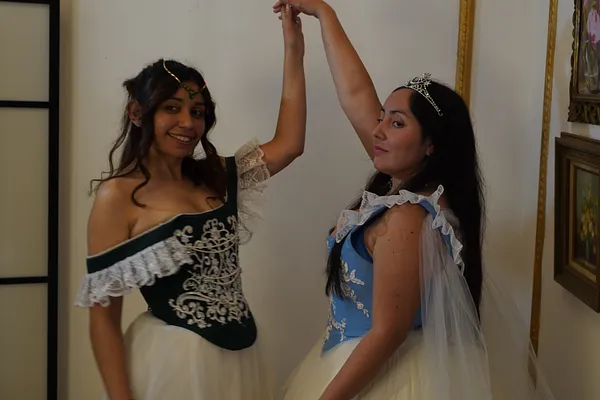 Dos modelos posando con vestidos de fantasía; Annie se ve con corpiño verde bordado, encaje blanco y falda voluminosa clara.