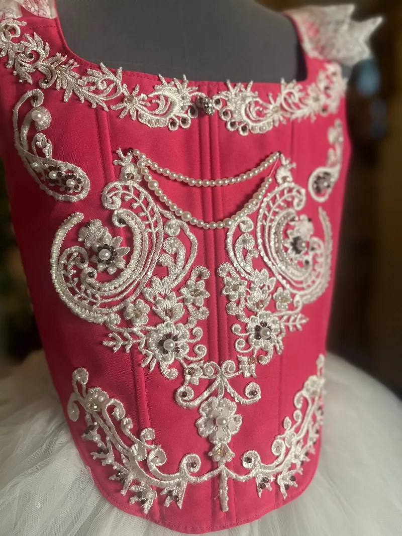 Detalle frontal del corpiño fucsia, cubierto con bordados plateados, aplicaciones florales, cuentas y cadenas decorativas sobre la tela satinada.