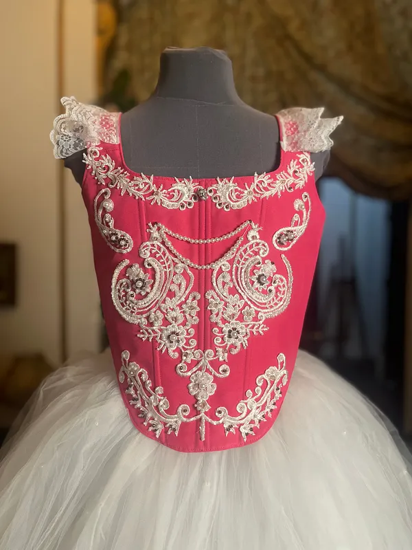 Vista frontal superior del vestido, con escote cuadrado, pequeñas mangas de encaje, ornamentación plateada simétrica y falda blanca de tul.