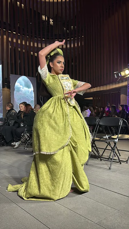Vista cercana de una bailarina con el vestido verde en pose escénica, mostrando el volumen de la sobrefalda, el panel frontal de encaje y las mangas con transparencias.